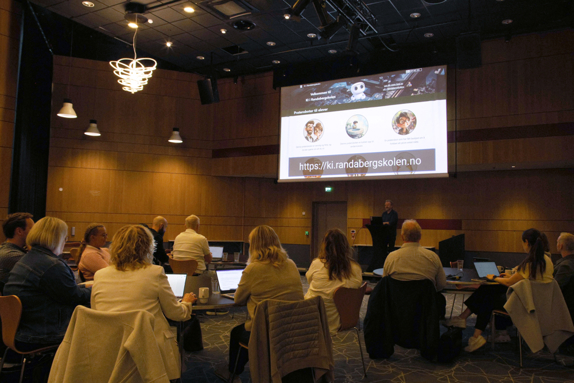 Odin Nøsen snakker foran, til folkene rundt bordene i salen.