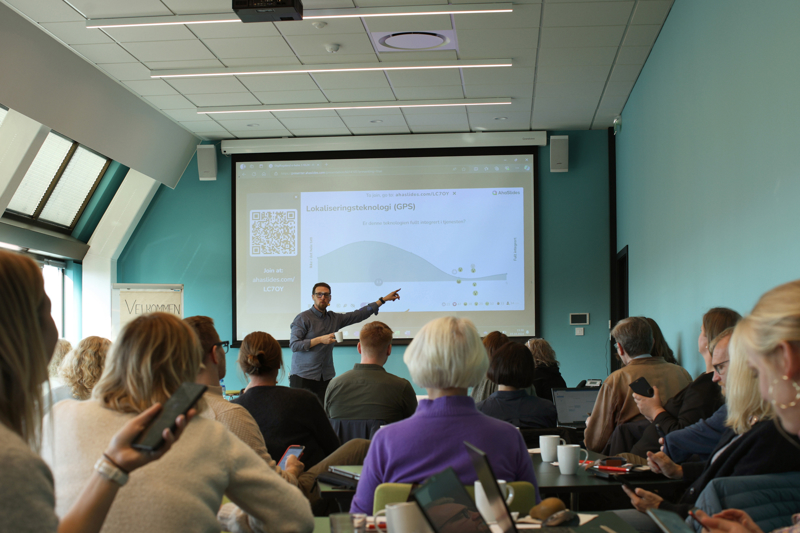 Arve står foran og peker på presentasjonen på skjermen, mens folkene i salen følger med.