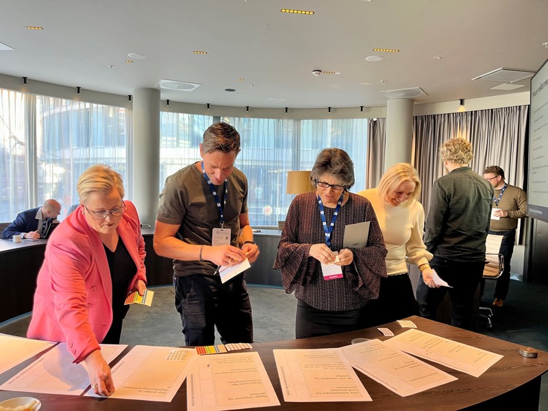 Vi ser fire av deltakerne som legger lapper på en bord. 