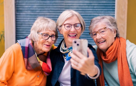 Illustrasjonsfoto fra Kakadu, viser noen blide damer som får hjelp med til å løse digitale utfordringer. De ser på en smart telefon.