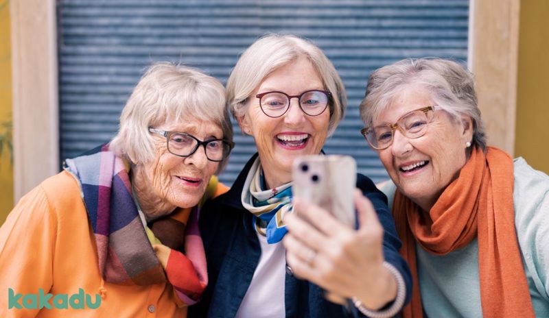 Bildet viser tre eldre damer som ser på en smarttelefon. 