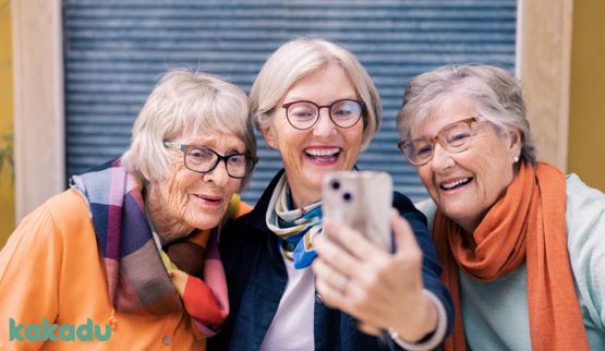 Bildet viser tre eldre damer som ser på en smarttelefon.