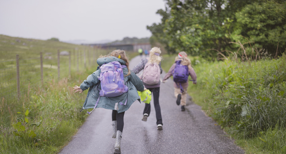 tre skolebarn løper på en vei i regnet